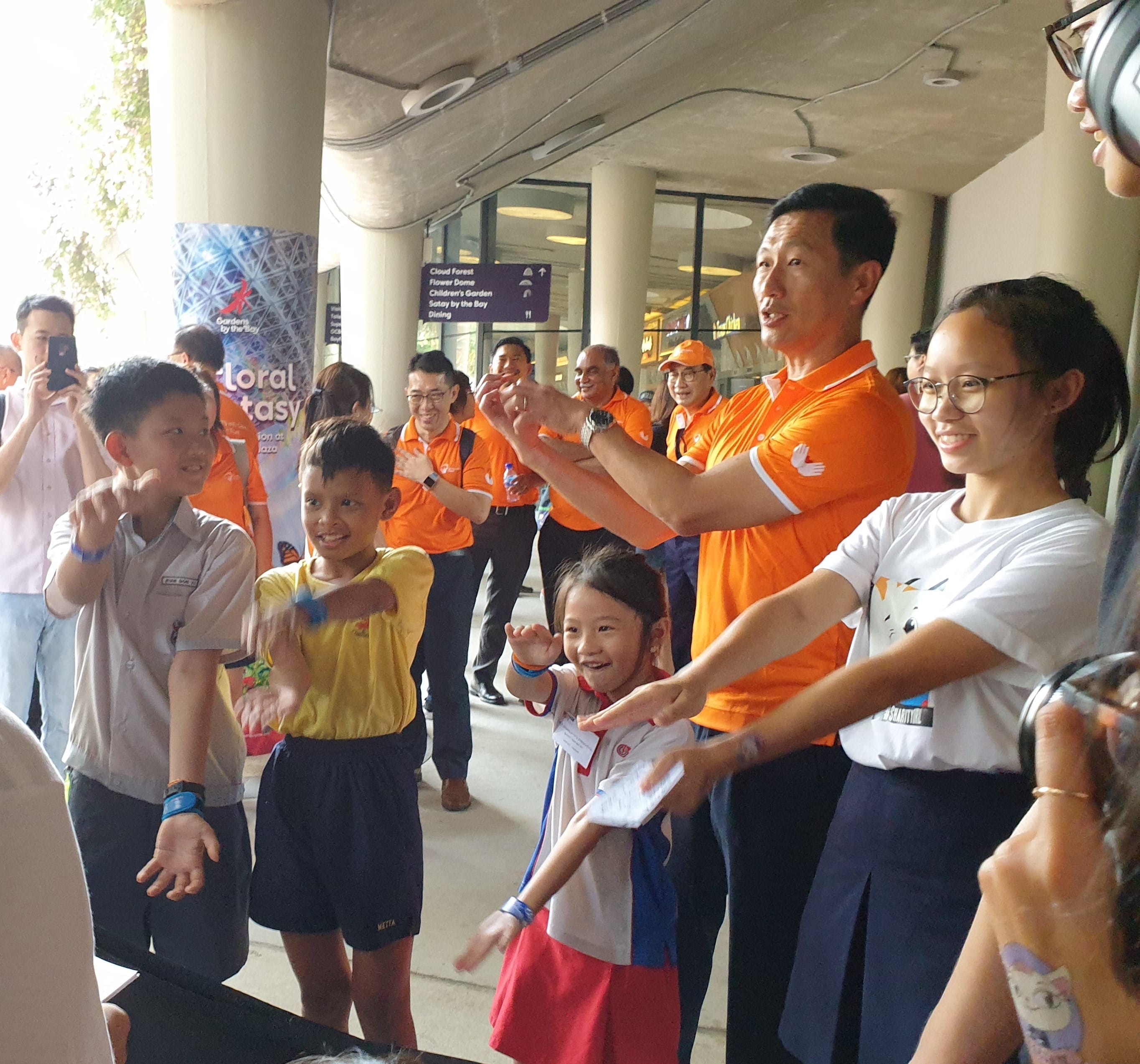 Adults in orange shirts and children laugh and gesture together outside Gardens by the Bay in Singapore.